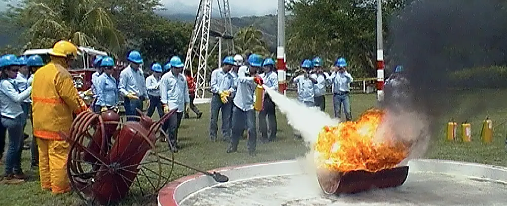 Estudiante con traje de protección apaga un fuego con una manguera mientras el grupo observa