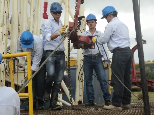 Estudiantes con casco azul trabajan con llaves de tubería en la plataforma del taladro de práctica