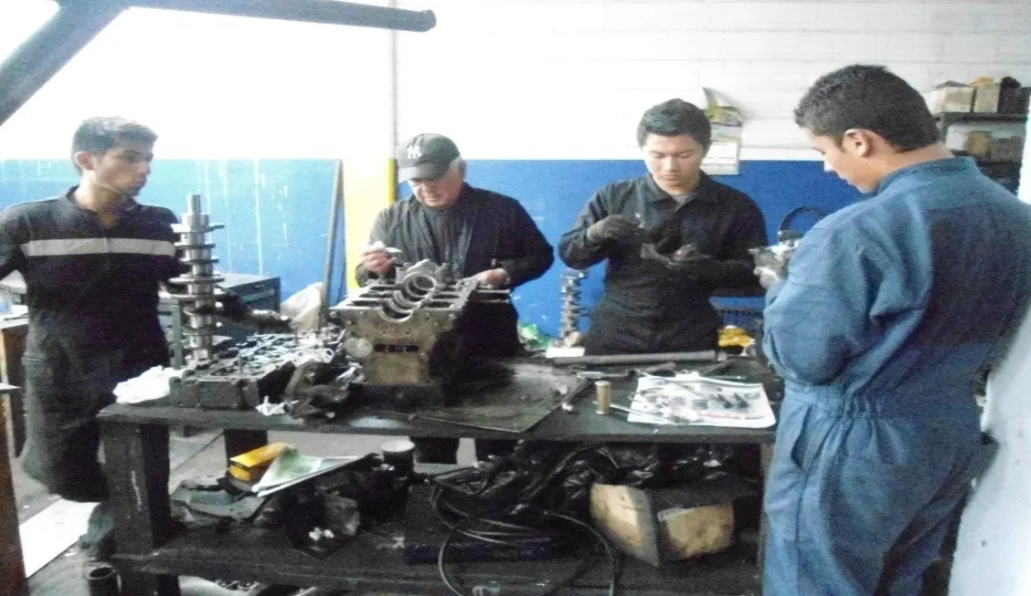 Estudiantes con overol trabajan con piezas de motor en el taller de mecánica