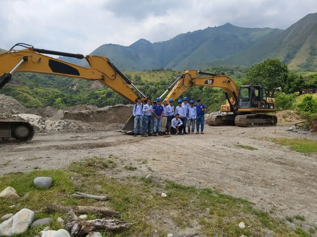 Grupo de estudiantes con casco junto a dos excavadoras durante una práctica de campo