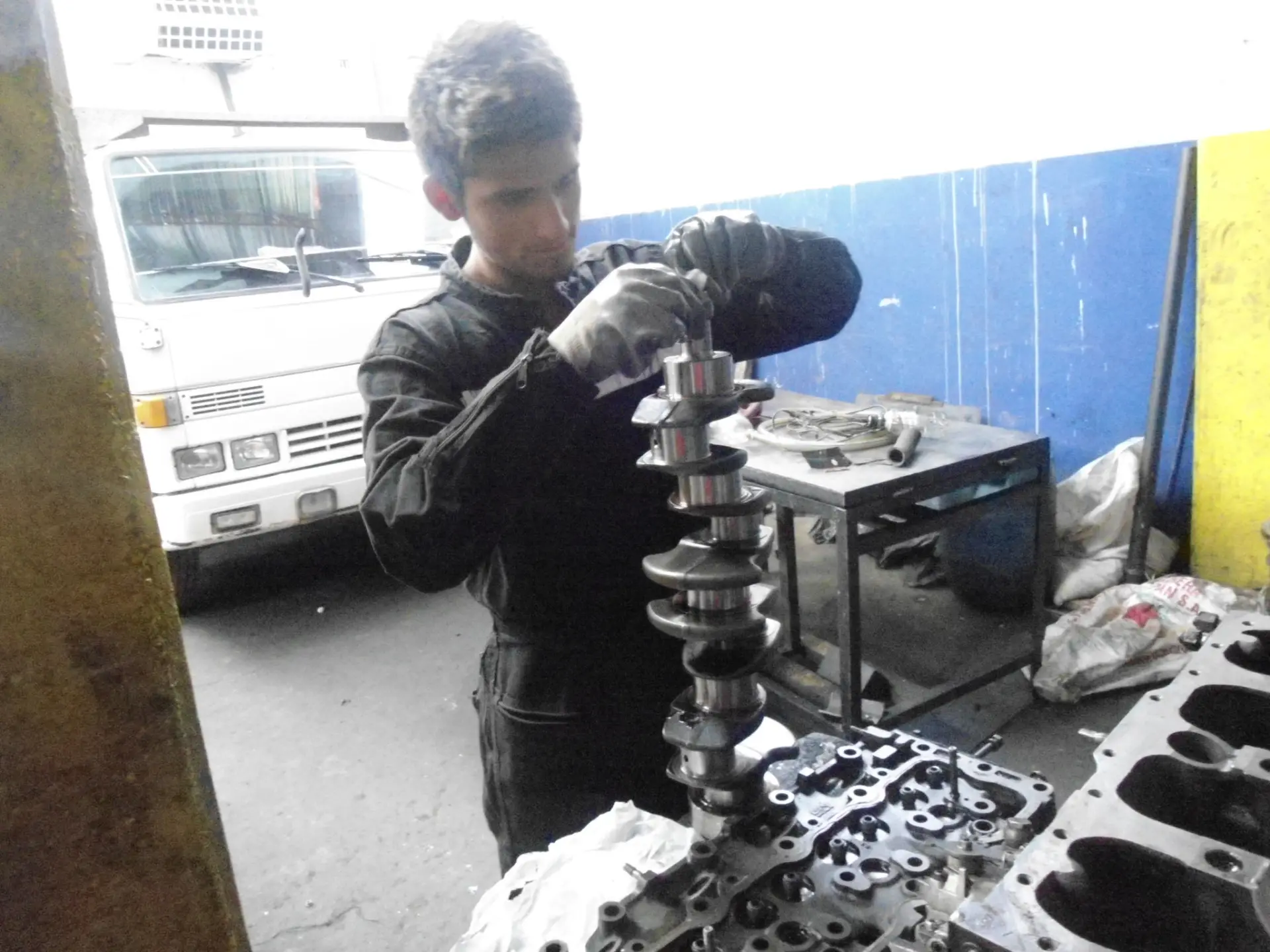 Estudiante con guantes revisa un cigüeñal sobre el banco del taller de mecánica