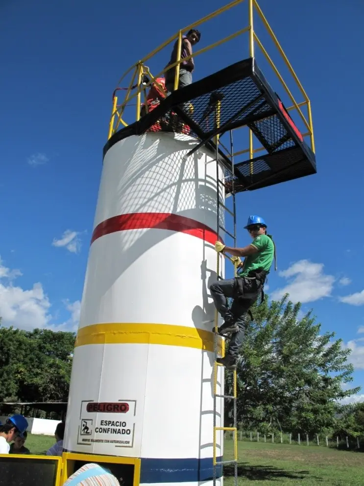Estudiante con casco y arnés sube por la escalera de la torre de práctica de espacios confinados
