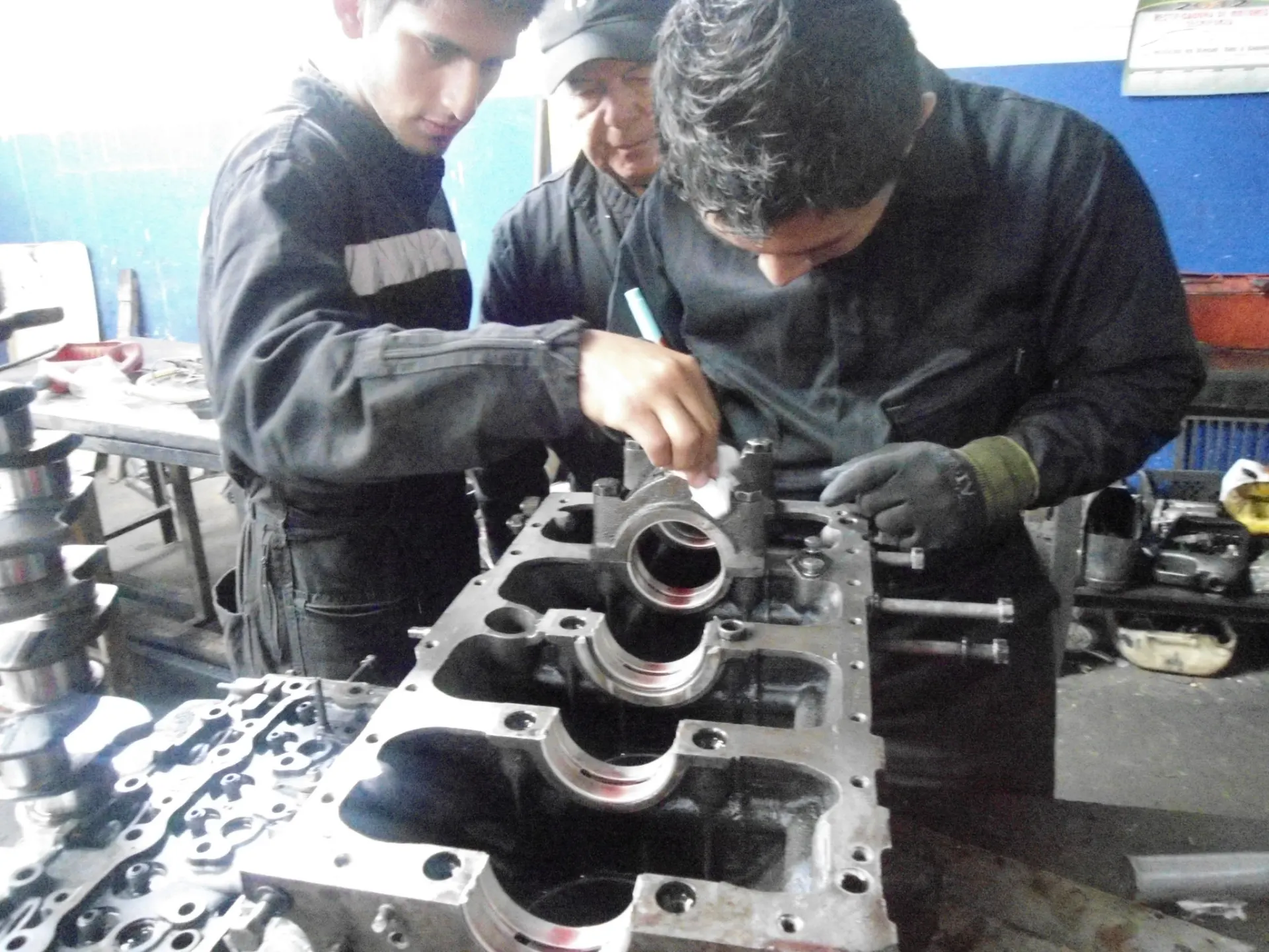 Estudiantes con guantes desarman el bloque de un motor en el taller de mecánica