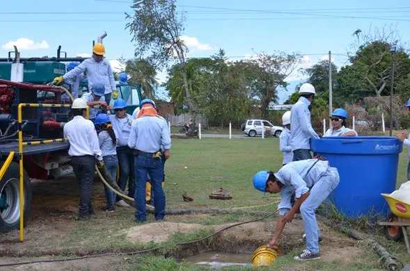 Estudiantes con casco trabajan con mangueras y un tanque junto al equipo de servicio a pozos de la escuela